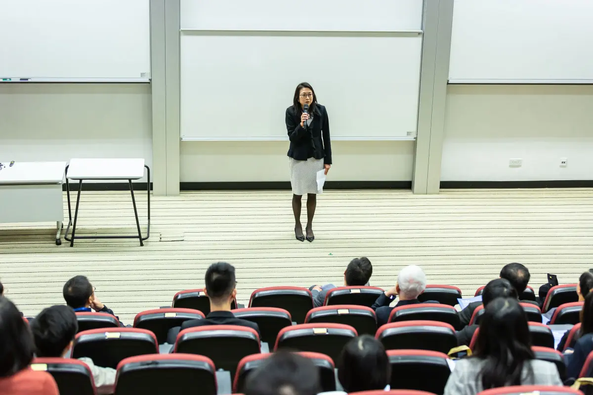 Seorang dosen berbicara di depan peserta di auditorium, seperti sesi microteaching di Kelas Luring